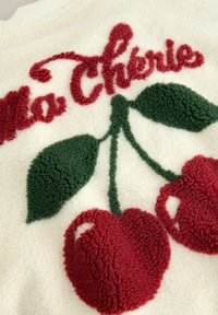 Fleece sweater featuring red cherry embroidery with green leaves on a cream background, "Ma Chérie" text in red plush texture.