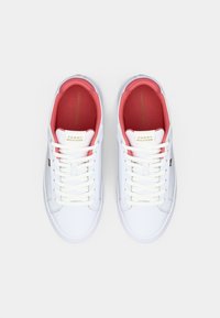 Balta Tommy Hilfiger sneakerių pora su koralinės rožinės spalvos vidiniu pamušalu ir baltais raišteliais, matoma iš viršaus ant vientiso fono.