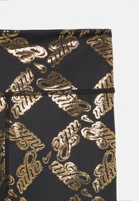 Tejido negro con un patrón dorado reflectante que cubre toda la superficie, con el texto estilizado "Nike". Textura suave; diseño ajustado con bordes sin costuras.