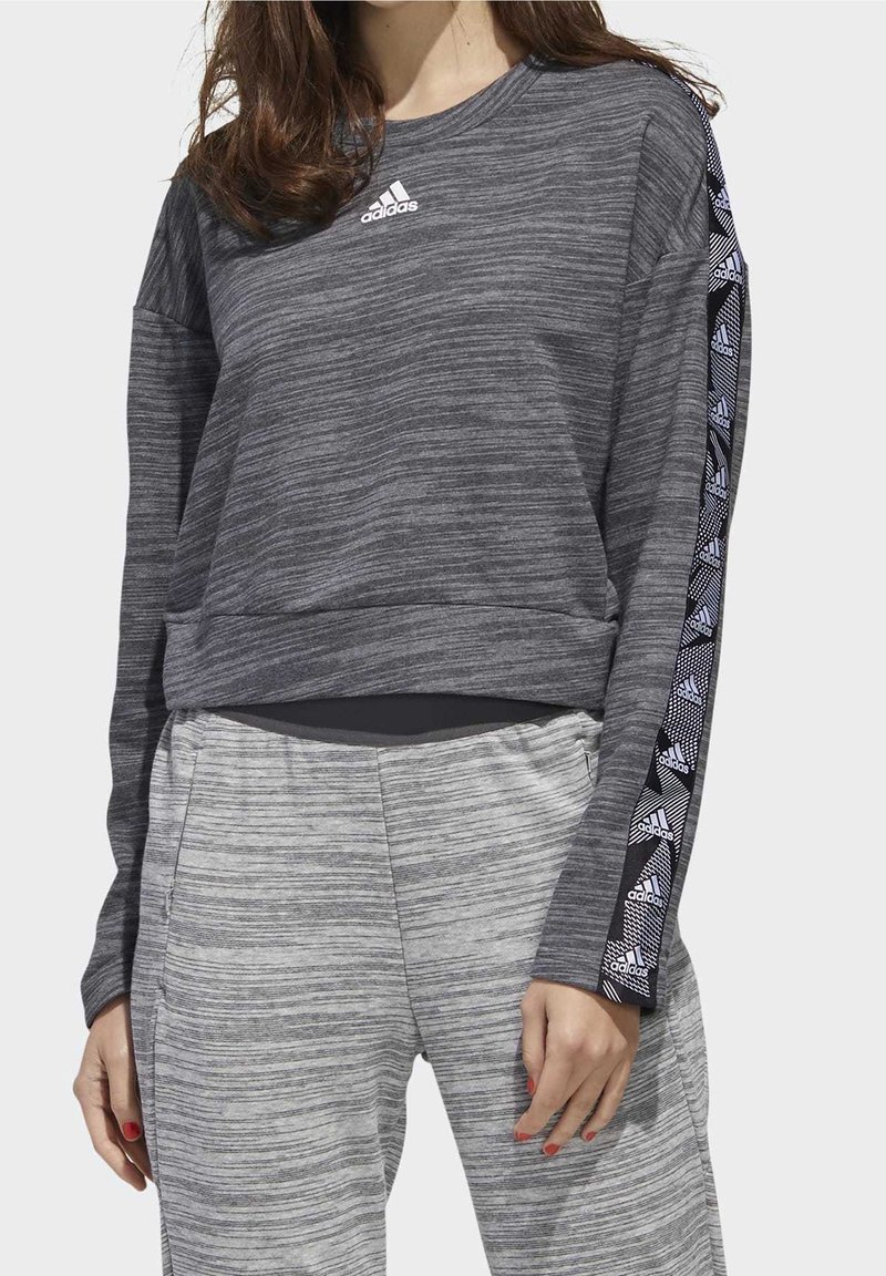 Sudadera gris de manga larga con un acabado texturizado y cuello redondo. Cuenta con rayas laterales de patrón contrastante y un logo de adidas en el pecho.