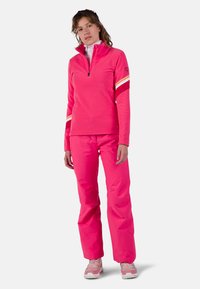 Fleece sweater en broek in felroze. De sweater heeft een halve rits, hoge kraag en gestreepte accenten op de mouwen. Glad textuur, sportieve pasvorm.