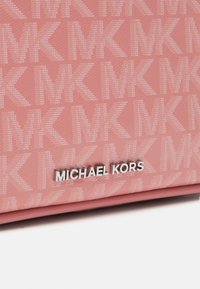 Różna, teksturowana tkanina z powtarzającym się wzorem "MK" oraz srebrnym logo Michael Kors umieszczonym w centrum dolnej krawędzi.