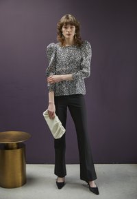 Blusa com padrão preto e branco, com mangas bufantes, calças pretas largas e uma carteira branca. Em fundo roxo.