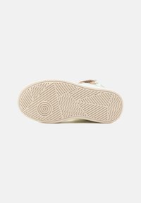 Semelle de chaussure de sport avec un motif texturé ; caoutchouc beige avec des lignes ondulées et des détails circulaires. Présente des accents vert clair sur les côtés.