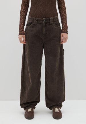 Los pantalones de pana marrones de pierna ancha presentan una cintura alta, bolsillos frontales y un bolsillo lateral. Combinados con zapatillas marrones y una blusa texturizada marrón.