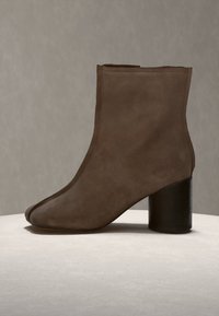 Bottine en daim marron avec bout arrondi et talon bloc noir épais sur surface claire et fond gris.