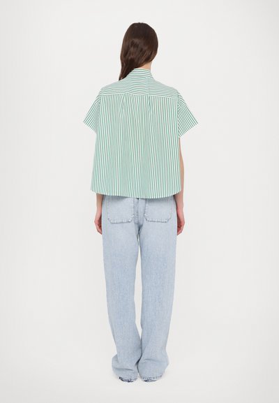 Green and white striped short-sleeve shirt with a loose fit and a curved back hem, paired with light blue wide-leg jeans.