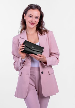 Schwarze Lederbrieftasche mit Klappenverschluss und silbernem Logodetail, gehalten von einer Person in einem pinken Blazer und passenden Hosen. Einfaches, elegantes Design.