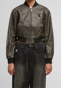 Veste bomber cintrée en simili cuir métallique gris avec des poignets et un ourlet côtelés. Comprend une fermeture éclair à l'avant, deux poches latérales et un logo brodé.