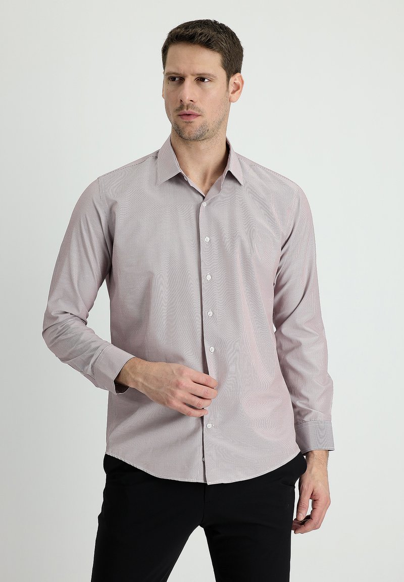Lichtroze knoopshirt met een subtiele gestreepte print, lange mouwen en een klassieke kraag. Gecombineerd met donkere broek.