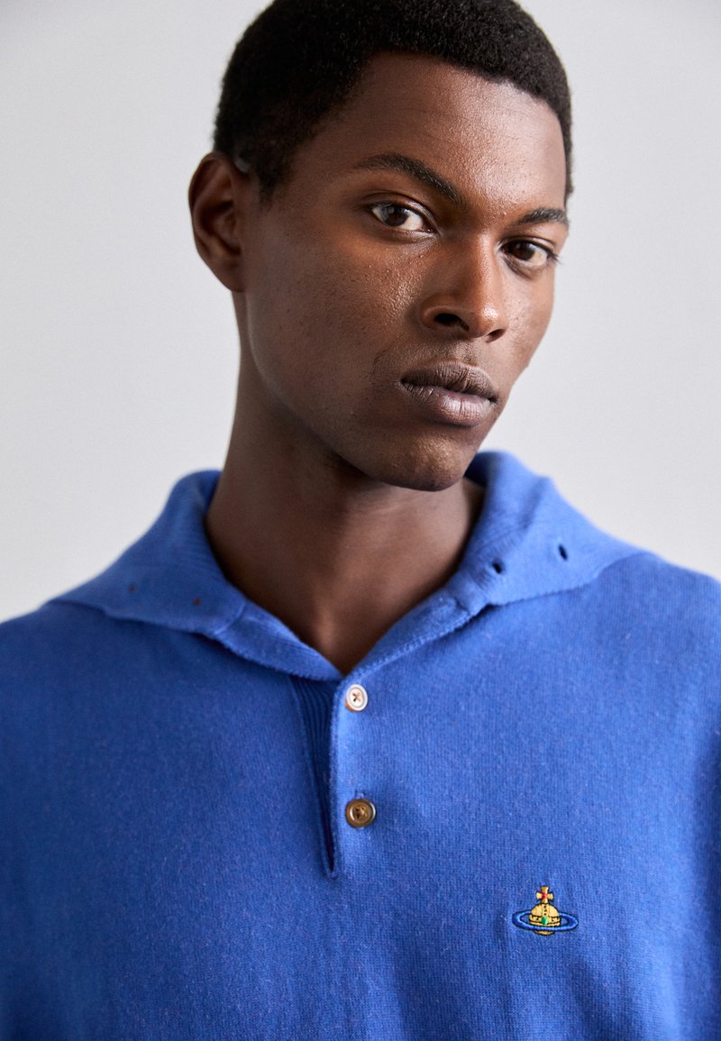 Blauwe gebreide pullover met een capuchon, voorzien van een knoopsluiting met twee knopen en een klein geborduurd ontwerp op de borst. Zachte textuur en een relaxte pasvorm.