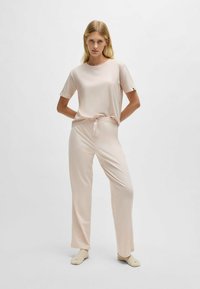 Ružový loungewear set s krátkym rukávom a okrúhlym výstrihom, doplnený voľnými nohavicami so sťahovacou šnúrkou, vyrobený z hladkej tkaniny.