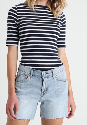 Woman wearing a navy and white striped short-sleeve top and light blue high-waisted denim shorts with frayed hems.