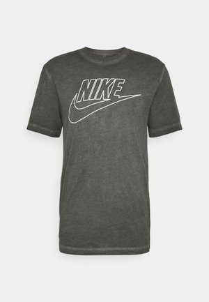 T-shirt en coton gris foncé avec un col rond et des manches courtes, arborant un grand logo Nike blanc sur le devant. Texture lisse.