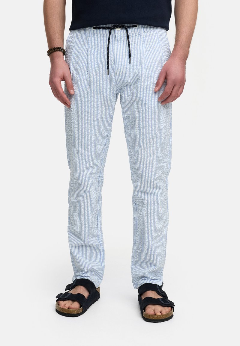 Pantalones de un azul claro con un patrón y un acabado texturizado, cintura con cordón, diseño de pierna recta, combinados con sandalias negras.