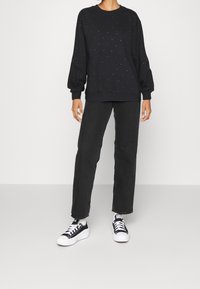 Černá mikina se stříbrnými cvočky, dlouhými rukávy a žebrovanými manžetami, kombinovaná s černými jeansy s rovnými nohavicemi a černo-bílými teniskami.