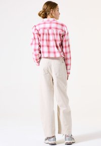 Kariertes rosa-weißes Flanellhemd mit lässiger Passform, kombiniert mit hellbeigen weit geschnittenen Hosen und grauen Sportschuhen.