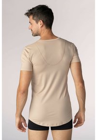 Beige kortärmad skjorta i slät tyg, med rundad halsringning och böjd söm på baksidan. Bärs tillsammans med svarta shorts.