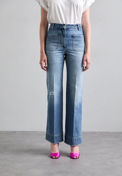 Jeans z wysokim stanem w niebieskim denimu o szerokich nogawkach i wybledzonym wykończeniu, z przednimi kieszeniami i surowym dołem, połączone z jasnoróżowymi butami odkrytymi na palcach.