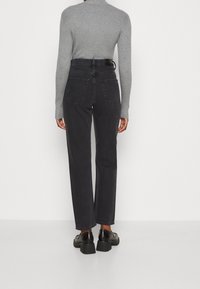 Jersey de cuello alto de canalé gris, vaqueros negros de tiro alto y pernera recta con dobles bolsillos traseros, combinados con mocasines negros gruesos.