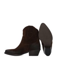 Brązowe kowbojskie buty zamszowe z zaostrzonym noskiem, niskim, warstwowym obcasem i ozdobnym przeszyciem na cholewce. Podeszwa zewnętrzna jest teksturowana.