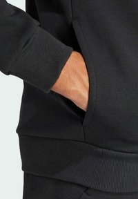 Felpa nera con polsini a costine e tasca laterale, caratterizzata da una texture liscia e un design aderente.