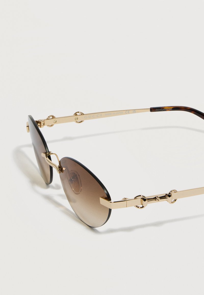 Lunettes de soleil à verres ronds marron dégradé avec montures en métal doré et détail mors de cheval sur les branches.