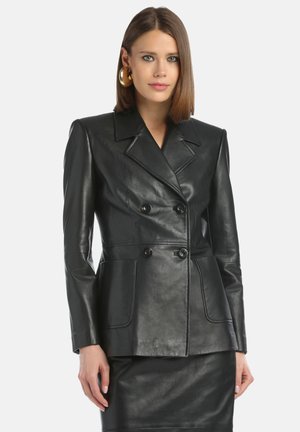 Blazer doppiopetto in pelle nera con colletto appuntito, tasche laterali e texture lucida, abbinato a una gonna in pelle coordinata.