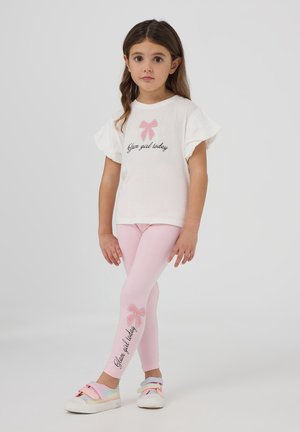 T-shirt bianco a maniche corte con una grafica a fiocco rosa e il testo "Glam girl today", abbinato a leggings rosa con un fiocco simile e dettagli di testo.