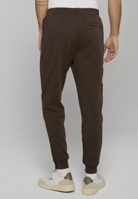 Bruine joggingbroek met zijstrepen, elastische tailleband en een achterzak, gecombineerd met witte sneakers met grijze accenten en veters.