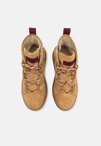 Bottes en suédine beige avec une doublure douce, munies d'accents rouges, de lacets à motifs et d'une fermeture éclair. Conçues pour le soutien de la cheville et le confort.