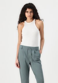 Hvit ribbet tanktop med høy hals, sammen med lysegrønne bukser med snøring og plisserte detaljer.