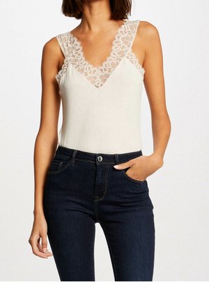 Body w kremowym kolorze z delikatną koronką wokół dekoltu w serek i ramiączek, w połączeniu z ciemnoniebieskimi dżinsami o dopasowanym kroju.