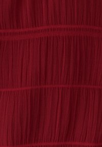 Rødt, letvægtsstof med en krøllet struktur og vandrette syningstråde, der skaber et lagdelt udseende.