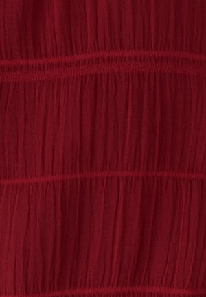 Punane, kerge kangas kortsus tekstuuriga ja horisontaalsete õmblusjoontega, luues kihilise välimuse.