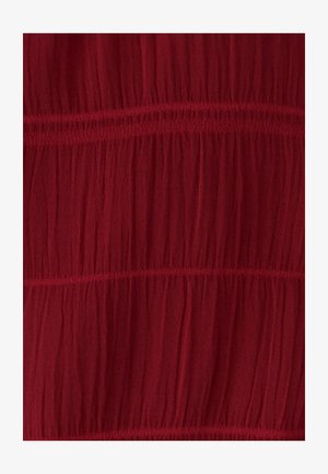 Červená, ľahká tkanina s vrásčitým povrchom a vodorovnými švami, ktoré vytvárajú vrstvený vzhľad.