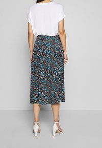 Blumiger Midirock mit dunklem Hintergrund und bunten Blumen, gefertigt aus leichtem Stoff, kombiniert mit einem einfachen weißen T-Shirt und Absätzen.