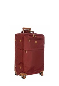 Valise en tissu rouge de forme rectangulaire, avec des poignées et des accents beige, deux poches avant et quatre roulettes rondes pour la mobilité.