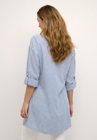 Triibuline tunika särk sinises ja valges, millel on rullitud varrukad ja kaardus hem. Kerge materjal ja mugav lõige.