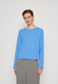 Camicia blu a maniche lunghe in tessuto leggero con scollo a girocollo, caratterizzata da un piccolo logo sul petto e un fit rilassato.