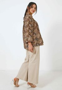 Brown snake print blouse with a collar and three-quarter sleeves, worn with beige wide-leg pants and clear heeled sandals.
