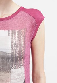 Lyhythihainen, vaaleanpunainen paita, jossa on teksturoitu graafinen printti abstrakteilla kuvioilla. Materiaali näyttää pehmeältä ja siinä on hieman kiiltoa.