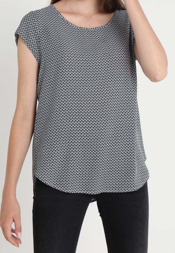 Blouse à manches courtes en noir et blanc avec un motif géométrique, un col arrondi et un ourlet courbé. Le tissu semble léger et lisse.