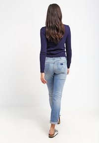 Jeans de denim azul con pierna ajustada, puños enrollados y bolsillos traseros. Se llevan con una camiseta de manga larga azul marino y sandalias planas.