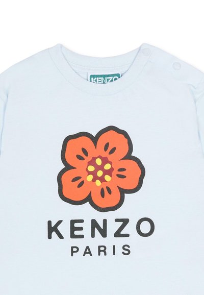 Chemise bleu clair à manches courtes avec un grand motif de fleur orange, détails jaunes au centre, et "KENZO PARIS" imprimé en noir en dessous.