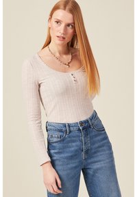 Helles, pinkes, geripptes Langarmoberteil mit einem gewellten Ausschnitt und drei Knöpfen, kombiniert mit hochtaillierten blauen Jeans.