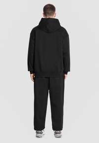 Czarna bluza z kapturem, o dużym kapturze, żebrowanymi mankietami i luźnym kroju, zestawiona z dopasowanymi czarnymi spodniami dresowymi. Teksturowany materiał; brak widocznych wzorów.