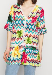Tunic colorata e stampata con scollatura a V e maniche svasate. Presenta disegni floreali e motivi a zigzag in tonalità vivaci. Bordata con pizzo.