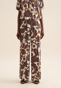 Pantaloni a gamba larga a motivi con una fantasia floreale in blu scuro e senape su uno sfondo chiaro. Realizzati in un tessuto leggero e morbido.