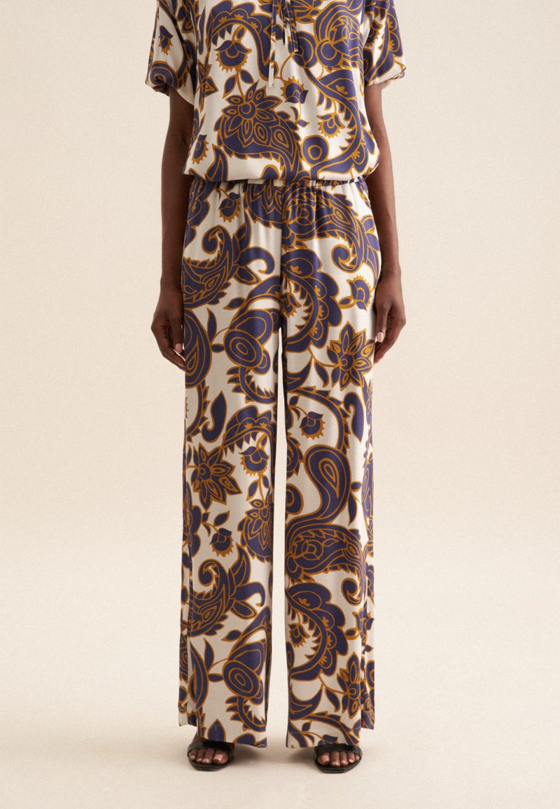 Pantaloni a gamba larga a motivi con una fantasia floreale in blu scuro e senape su uno sfondo chiaro. Realizzati in un tessuto leggero e morbido.